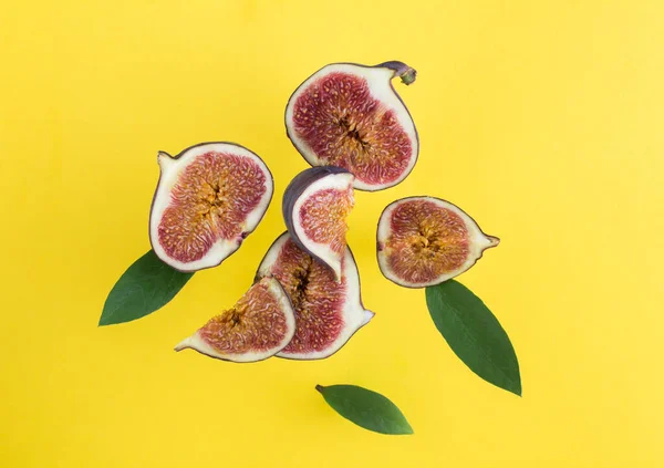 Flying in air fresh ripe whole and cut blue figs with leaves on the yellow background. Top view. Close-up.