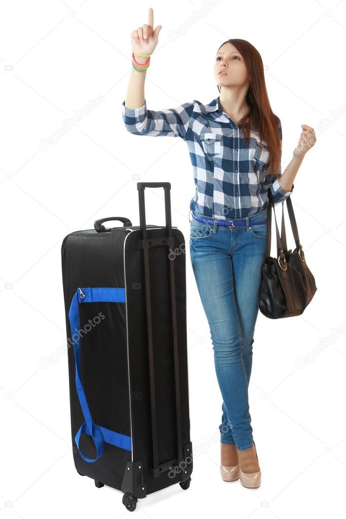 A young girl with a big, black travel bag on wheels, looks timetable in a station. Teen girl 16 years old, with a big, black travel bag on wheels. One person, teenager, female, isolated, vertical.