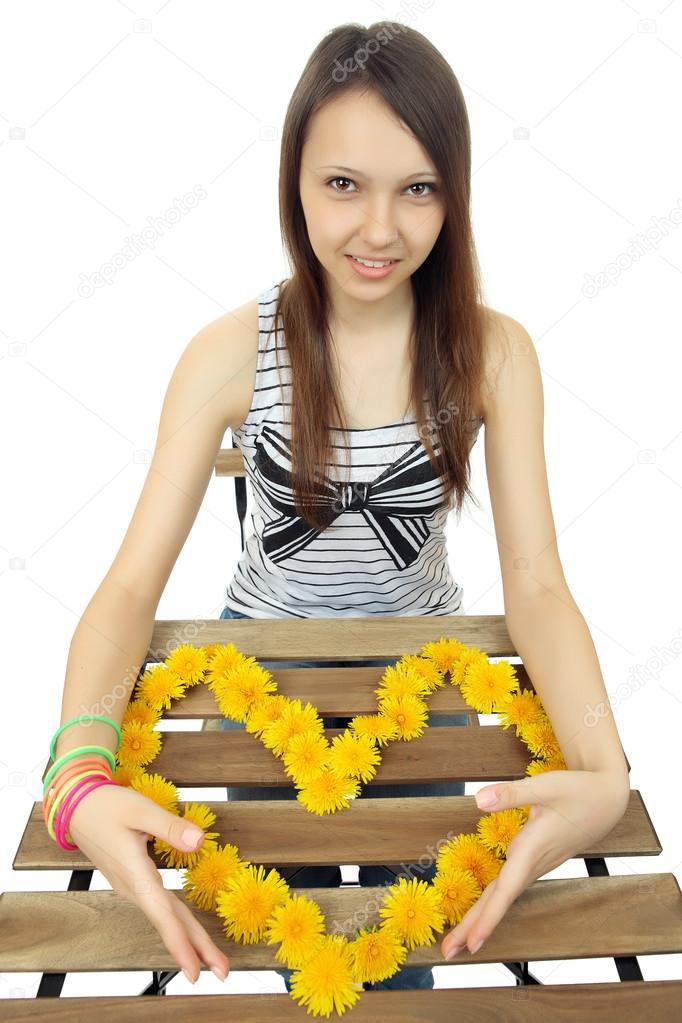 The girl shows the heart of wildflowers. Heart of yellow dandelions. To lay out the heart from flowers. One Caucasian teen girl 16 years old, holds a heart of yellow dandelion flowers. One person.