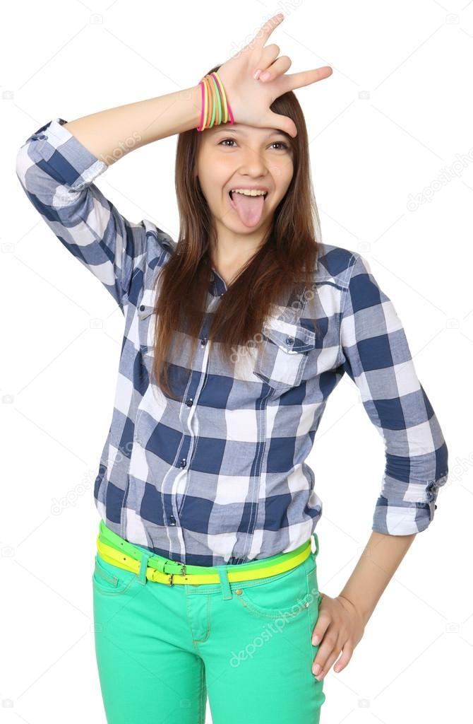 Teenage girl shows tongue and makes hand horns. Mint-colored pants and a plaid shirt.