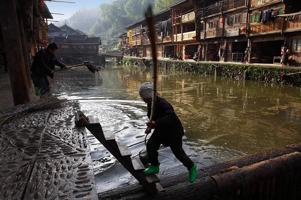 Río en la aldea Zhaohing GUIZHOU CHINA: La mujer étnica Dong elimina los escombros de la superficie de la aldea del río, el hombre en tela de lavado del río para lavar el terraplén de la aldea del río Zhaoxing Dong Village, abril de 2010 — Foto de Stock