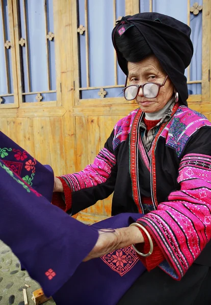 Old woman with big glasses, red Yao nationality, ethnic minorities in China, holding a blue cloth with patterns embroidered by hand, 4 April 2010. Xiaozhai Yao ethnic minority village, near Longsheng — Stock Photo, Image