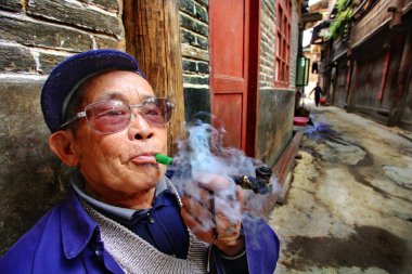 Çinli köylü bir tüp daha önce evinin içiyor. Çinli adamın yaşı boru ve bültenleri tütün dumanı füme. 9 Nisan 2010. zhaoxing dong etnik azınlık köyleri, liping İlçesi. Guizhou, Çin.