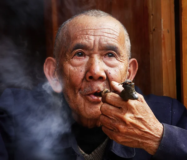 Il contadino cinese fuma un tubo davanti a casa sua. Invecchiato cinese acceso il suo portatile e lasciare che un fumo di tabacco. 9 aprile 2010. Zhaoxing Dong villaggio delle minoranze etniche, Liping County. PROVINCIA DI GUIZHOU, CINA — Foto Stock