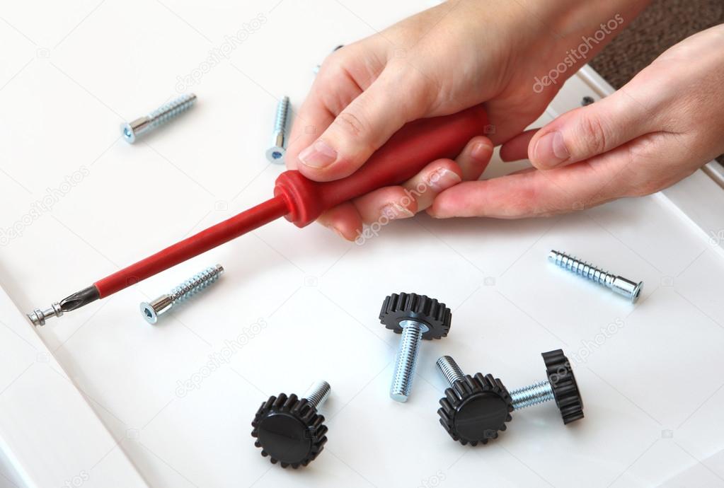 Assembling furniture, hand with screwdriver, adjustable plastic legs with screw.