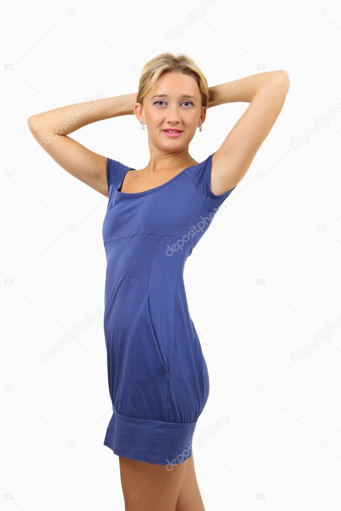 Woman in short, skin-tight, blue dress, holds hands behind her head.