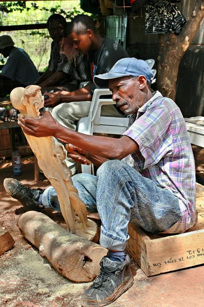 Art workshop outdoors woodcarver carves Maasai figurines. — Stock Photo, Image