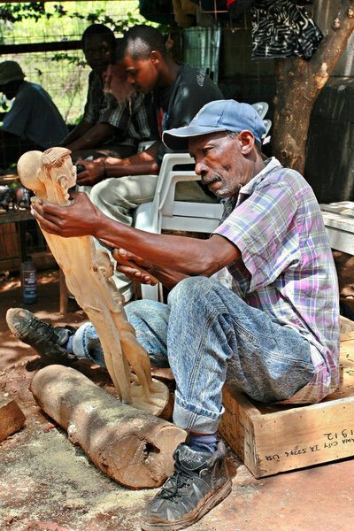 Art workshop outdoors woodcarver carves Maasai figurines.
