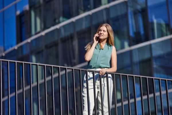 Kadın yönetici cam iş merkezi yakınında telefonla konuşuyor..