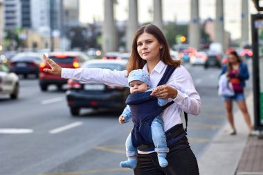 Bebek askılı anne trafiğin yanında taksiyi durduruyor..