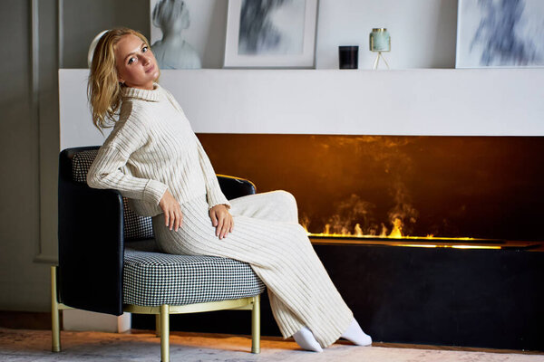 Молодая белая женщина сидит у камина дома.