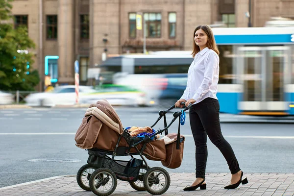 Femme avec bébé en landau marche près de la circulation dans la rue de la ville. — Photo