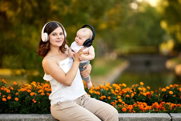 Kvinna i trådlösa hörlurar sitter i parken med barnet under mammaledigheten. — Stockfoto