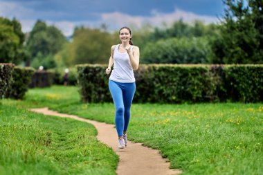 Spor giyimli mutlu kadın parkta koşuyor..