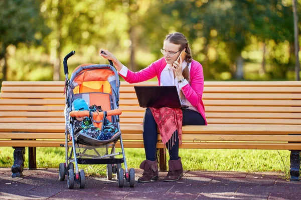 Woman with infant in pram is talking by phone outdoors. — Stock Photo, Image