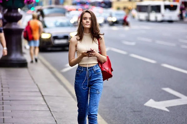 Slim nő sétál az utcán a forgalom és tartja okostelefon. — Stock Fotó