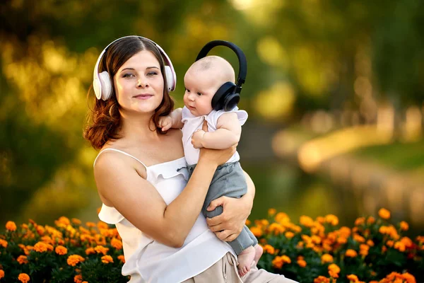 Kvinna med spädbarn lyssnar på musik med trådlösa hörlurar utomhus. — Stockfoto