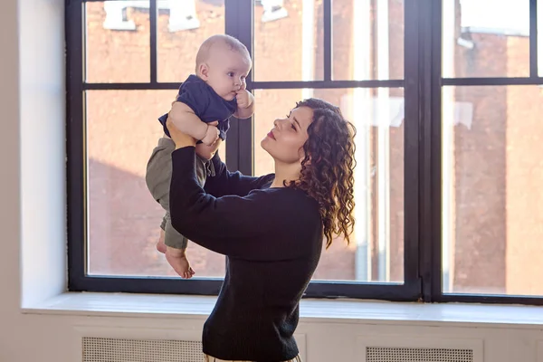 Femme se tient près de la fenêtre avec un petit garçon dans les mains. — Photo