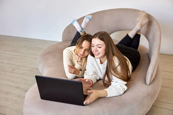 Mulheres sorridentes olham para o laptop enquanto se deitam no sofá no salão. — Fotografia de Stock
