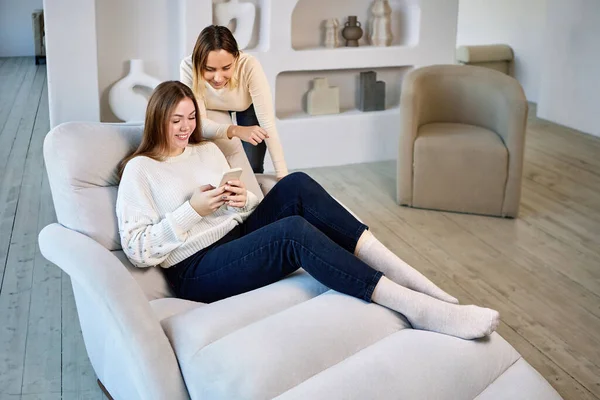Two women on chaise longue with phone in lounge. — Stock Photo, Image