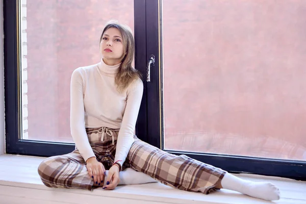 Jeune femme en pantalon à carreaux assis sur le rebord de la fenêtre. — Photo