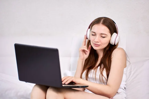 Kvinna i hörlurar med bärbar dator lyssnar på musik i sängen. — Stockfoto