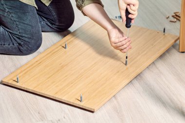 Tamirci tornavida yardımıyla düz paket mobilya monte ediyor..