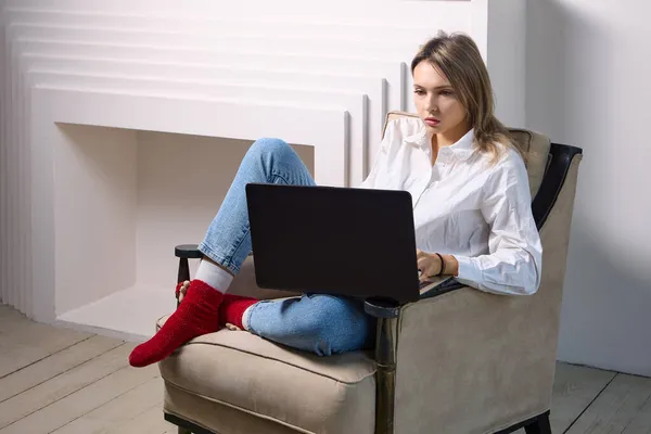 Kobieta z laptopem siedzi w fotelu we wnętrzu salonu. — Zdjęcie stockowe