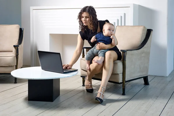 Mère tient bébé tout en faisant du travail à distance en utilisant un ordinateur portable. — Photo