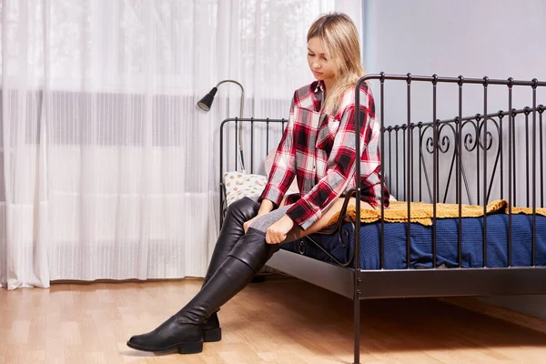 Nad kolana buty jest ubrany przez kobietę na łóżku wewnątrz. — Zdjęcie stockowe