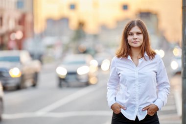 Sokak trafiğinin arka planında beyaz gömlekli bir kadın var..
