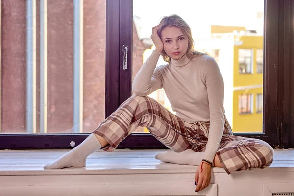 24岁的老妇人穿着格子呢裤子，坐在家里的窗台上. — 图库照片