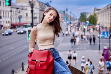 Kalabalık şehir sokağının önünde, araba trafiği olan ince bir bayanın yanında kırmızı çanta..