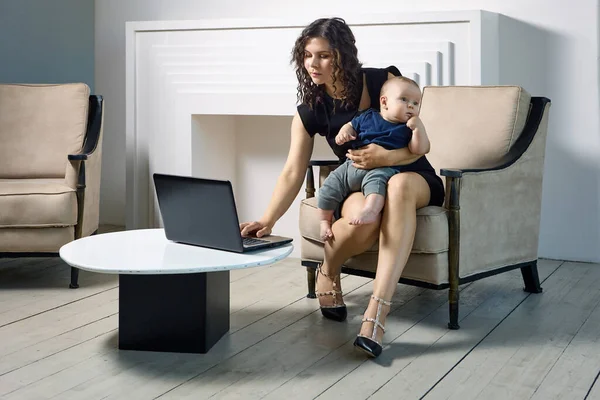 Žena na mateřské dovolené pracuje na dálku, s dítětem na kolenou. — Stock fotografie