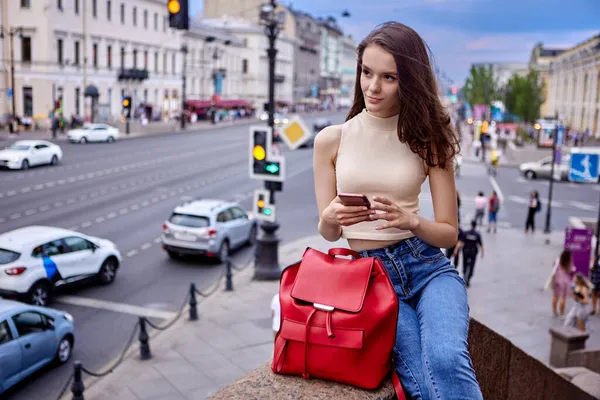 Grote rode leren tas wordt vastgehouden door slanke vrouwelijke student in jeans en top wandelen door drukke avond stad op de zomeravond. — Stockfoto