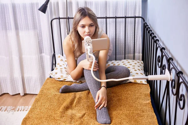 Hem telefonhållare med klämma fäst på sängen, ung vit kvinna tittar på film på smartphone-skärmen. — Stockfoto