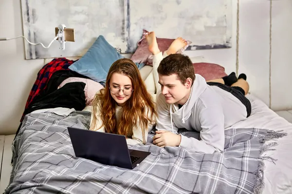 Video Conferentie van vrienden met behulp van laptop, jong Europees paar liggen op bed voor het scherm in hun slaapkamer. — Stockfoto