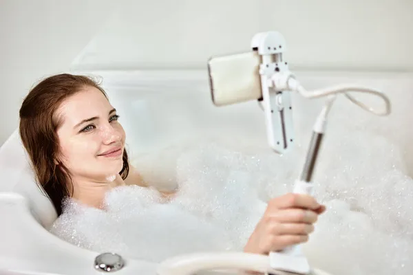 In der Badewanne liegend, macht Frau Videoanruf, indem sie Handy in Halterung fixiert. — Stockfoto