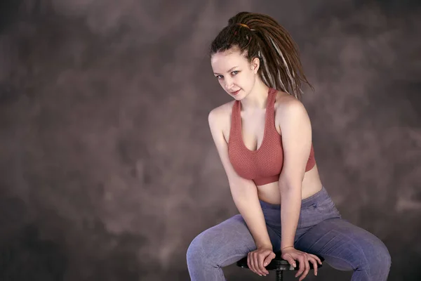 Mujer de 28 años con trenzas de caja se sienta en el taburete de la barra con camiseta y jeans. —  Fotos de Stock