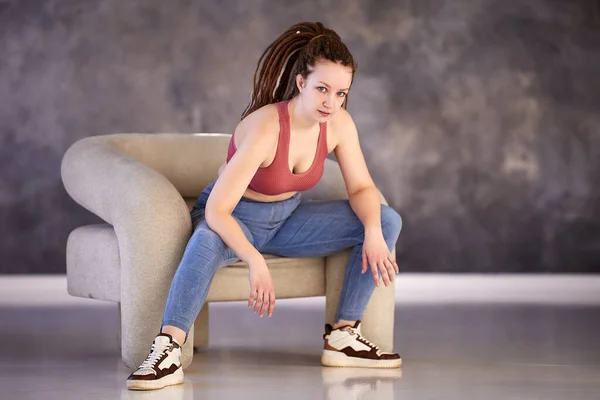 Mujer blanca de 28 años con trenzas box en su peinado se sienta en un sillón de estudio de danza. —  Fotos de Stock
