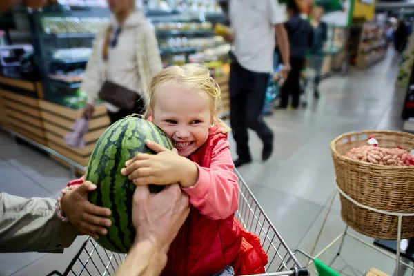 Ler liten flicka med vattenmelon sitter i stormarknad vagn. — Stockfoto