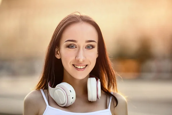 Glad ung kvinna med sladdlösa hörlurar på halsen utanför. — Stockfoto