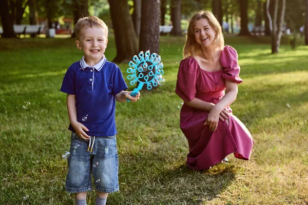 Smiling mother with son play with bubbles outside. — Stock Photo, Image
