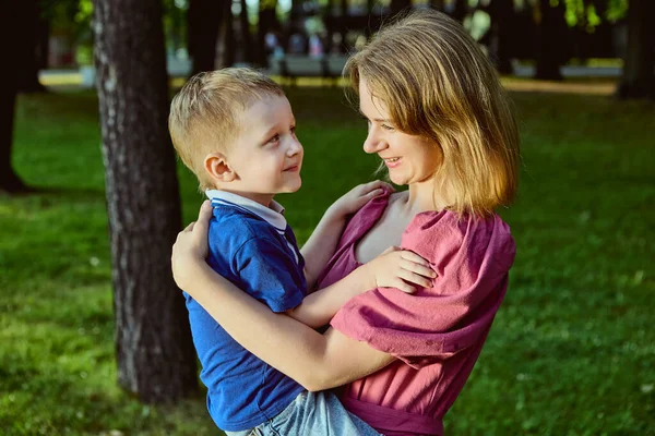 Moeder knuffelt kleine jongen in park terwijl hebben rust. Stockfoto