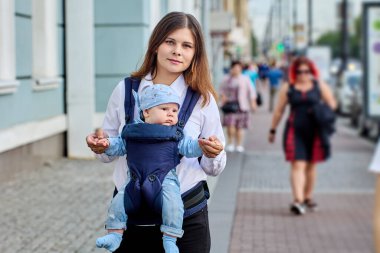 Annesi tarafından şehir sokaklarında tutulan küçük çocukla bebek askısı..