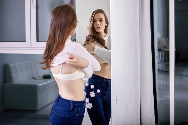 젊은 여자가 거울 근처에서 옷을 갈아입는다. — 스톡 사진