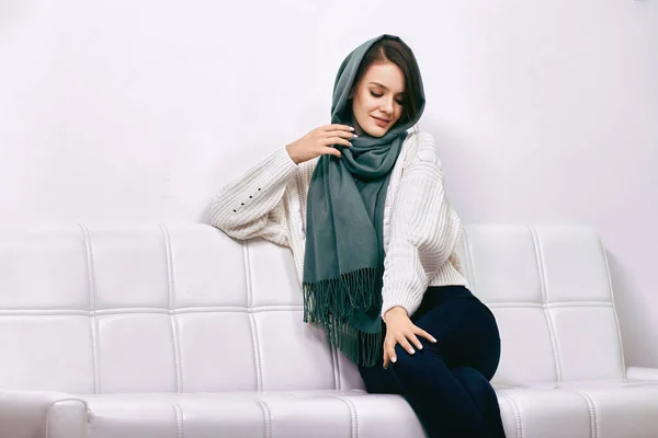 Young woman 20 years old in headscarf sits on couch inside. — Stock Photo, Image