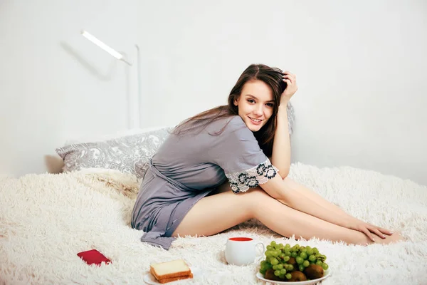 Jeune femme en peignoir a le petit déjeuner au lit à l'intérieur. — Photo