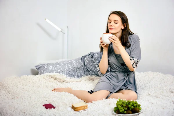 Káva ráno v posteli od ženy 20 let v županu. — Stock fotografie