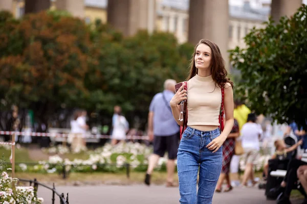 Slender woman stands on city street in jeans at daytime. — Stock Photo, Image